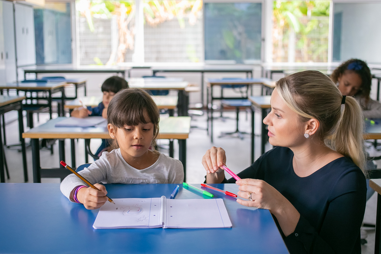 Serious Primary School Teacher Helping Girl Cope With Her Task